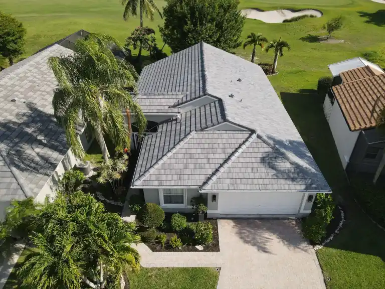 Gray tile roof over a narrow one-story house with a brick driveway and a golf course behind in Greenacres, completed May 2025