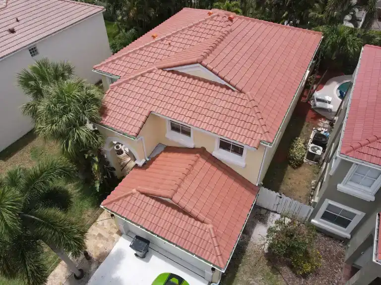 Red tile roof with a small triangular inset on a two-story house above a lower garage roof in Greenacres, photographed May 2025