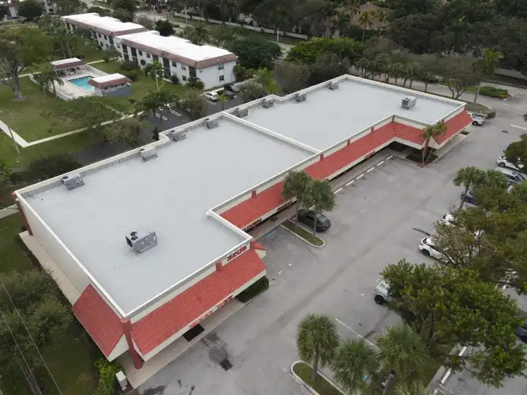 White flat roof over an L-shaped shopping plaza with red tile awnings and an almost empty parking lot in Delray Beach, completed November 2024